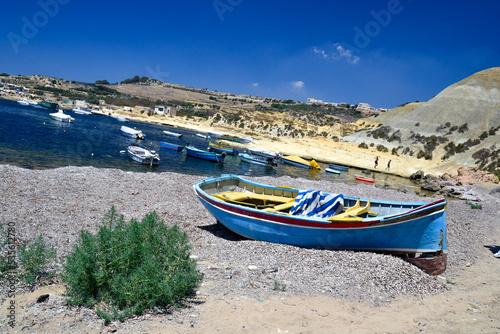 Small traditional Maltese boat on the beach in front of a harbor