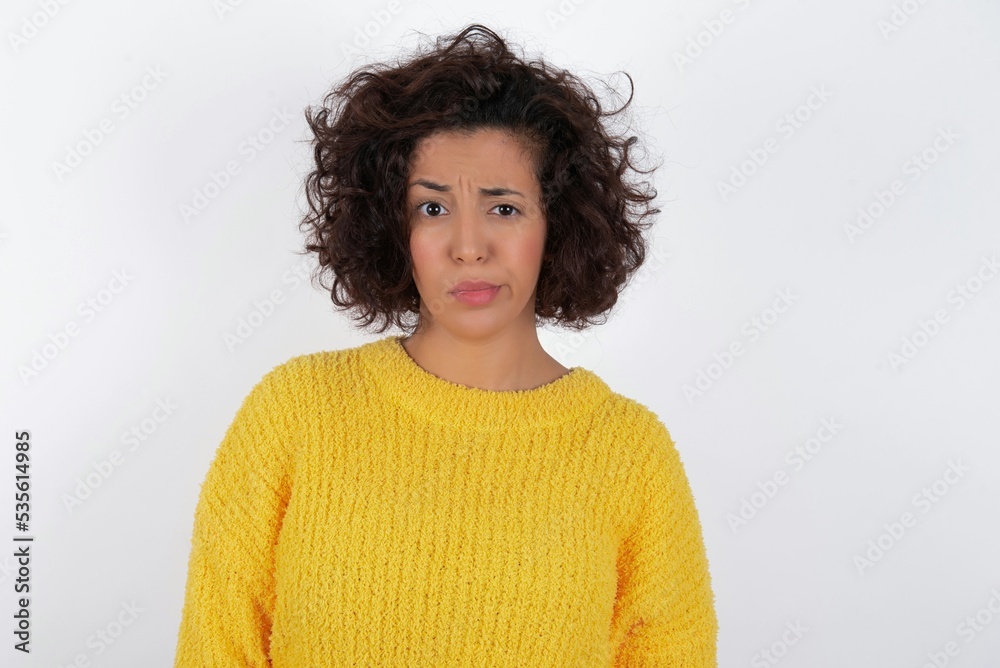 Displeased young beautiful woman with curly short hair wearing yellow sweater over white background frowns face feels unhappy has some problems. Negative emotions and feelings concept Displeased young beautiful woman with curly short hair wearing yellow sweater over white background frowns face feels unhappy has some problems. Negative emotions and feelings concept