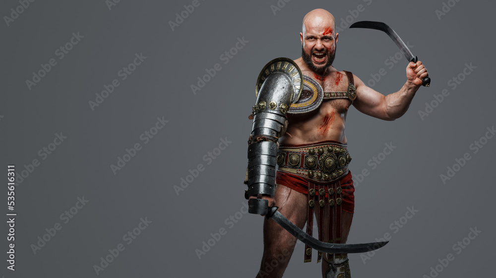 Portrait fo violent ancient gladiator screaming holding two swords against grey background. Portrait fo violent ancient gladiator screaming holding two swords against grey background.
