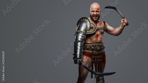 Portrait fo violent ancient gladiator screaming holding two swords against grey background.