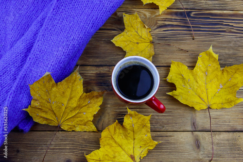 Cosy knitted blue sweater, cup of coffee and autumn maple leaves on wooden table. Top view. Autumn cozy concept