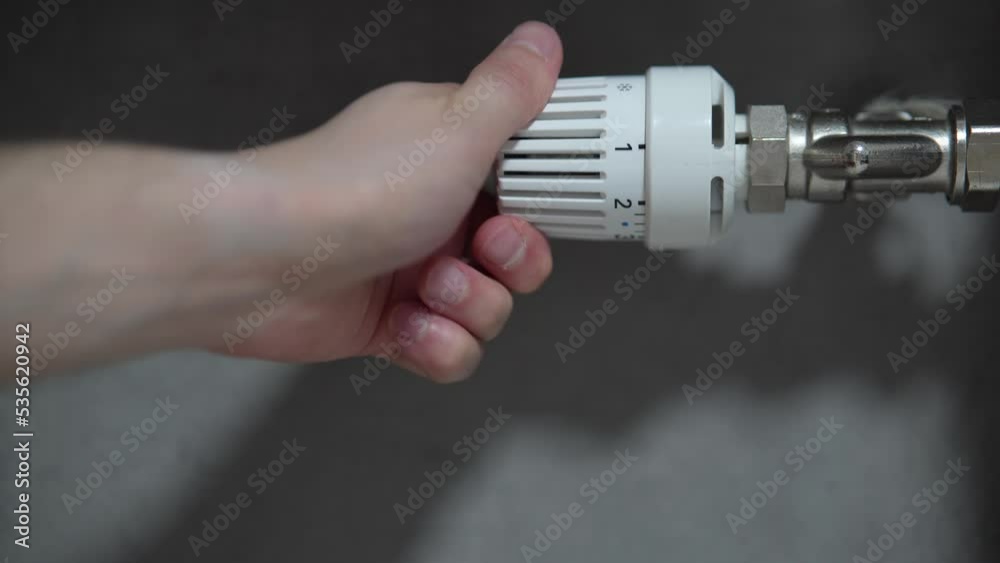Hand adjusting temperature on heating radiator thermostat, saving energy by adjusting heating thermostat. Hand adjusting temperature on heating radiator thermostat, saving energy by adjusting heating thermostat.