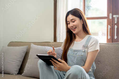 Young woman is listening music and watching movie on tablet while sitting on comfortable the couch