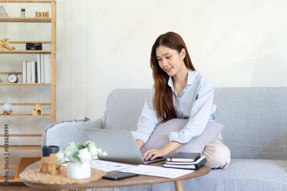 Female freelance is reading business data and typing information on laptop while sitting on comfortable Female freelance is reading business data and typing information on laptop while sitting on comfortable