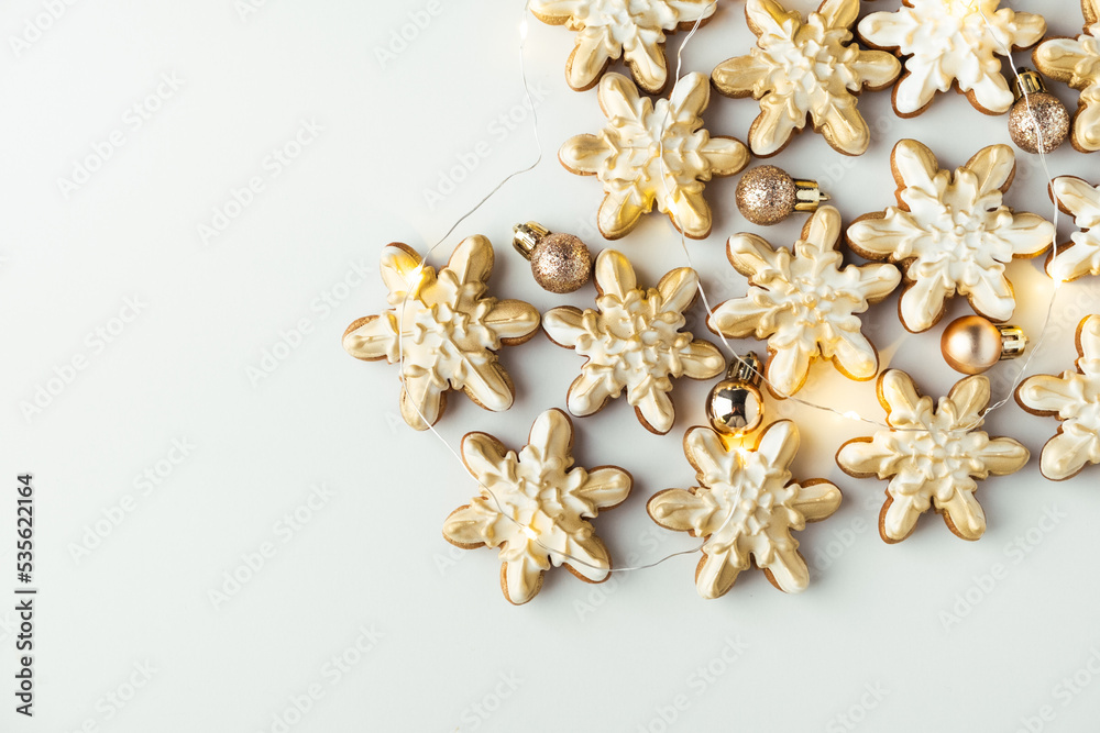 Snowflake shaped gingerbread cookies with golden festive icing. Christmas cookies with garland lights on white background. Happy New Year. Flat lay. Snowflake shaped gingerbread cookies with golden festive icing. Christmas cookies with garland lights on white background. Happy New Year. Flat lay.