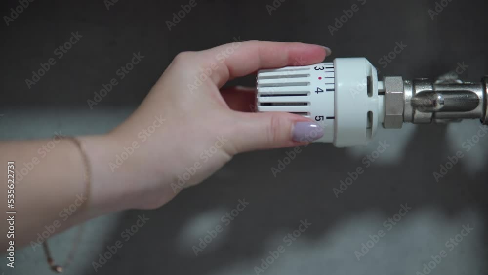 Hand adjusting temperature on heating radiator thermostat, saving energy by adjusting heating thermostat. Hand adjusting temperature on heating radiator thermostat, saving energy by adjusting heating thermostat.