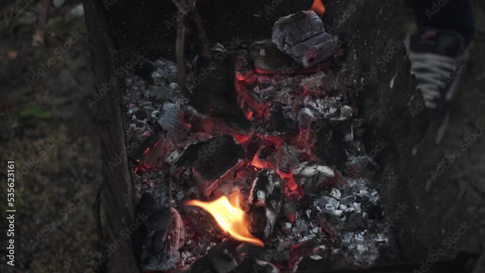 a man stirs smoldering burning coals in the brazier with a stick, sparks fly. shooting close-up, slow motion, summer motifs a man stirs smoldering burning coals in the brazier with a stick, sparks fly. shooting close-up, slow motion, summer motifs