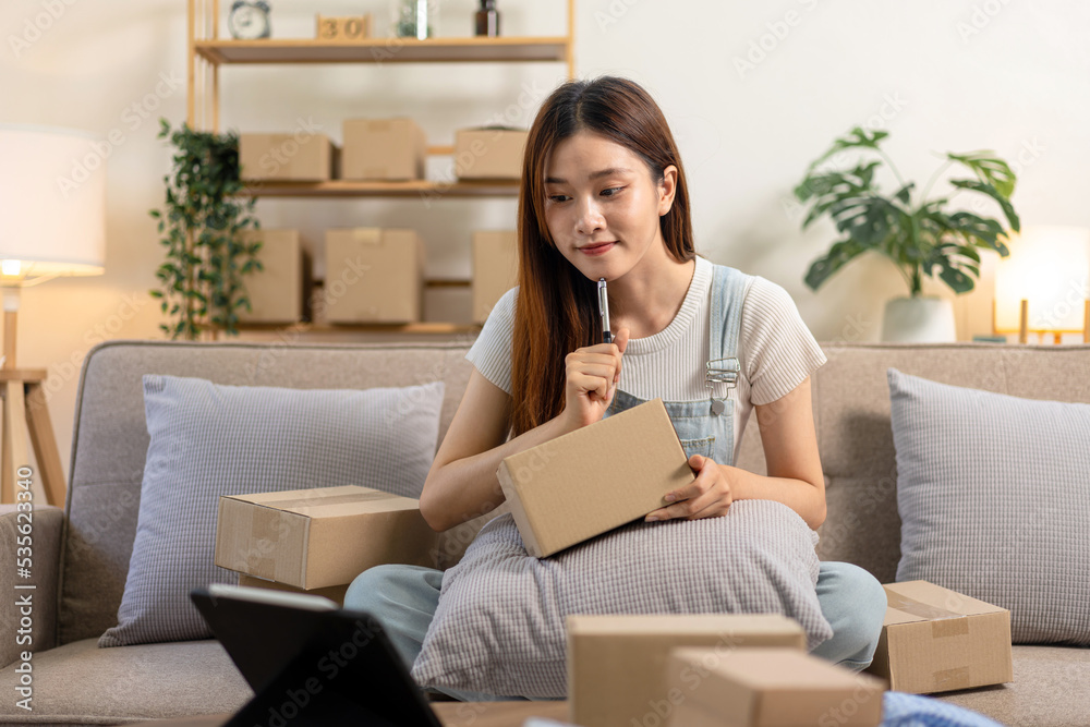 Young entrepreneur is using tablet to checking online orders and writing customer address on cardboard boxes Young entrepreneur is using tablet to checking online orders and writing customer address on cardboard boxes