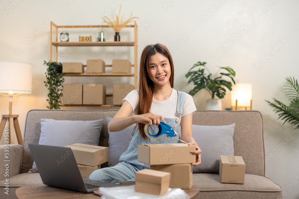 Young entrepreneur is packing clothes into cardboard boxes and using tape to seal for home delivery Young entrepreneur is packing clothes into cardboard boxes and using tape to seal for home delivery