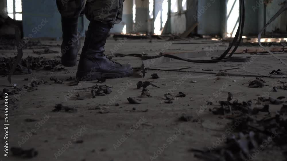 A stalker soldier in army boots walks through an abandoned factory, close-up of his legs. Post-apocalyptic concept
