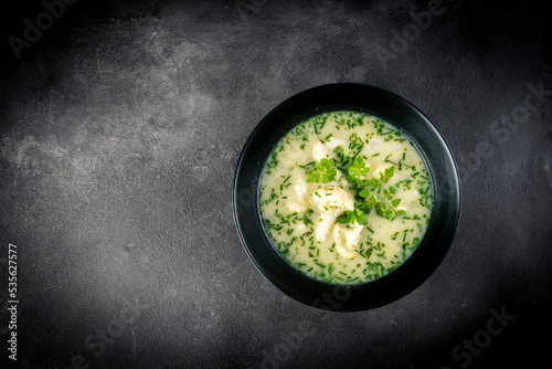 Cauliflower cream soup garnished with chives, chervil and marjoram, on a dark grey stone background