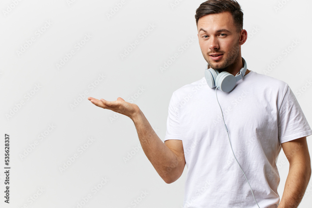 Smiling tanned handsome man in basic t-shirt headphones hold invisible object for ad posing isolated on over white studio background. Copy space Banner Mockup. Favorite song Music platform concept
