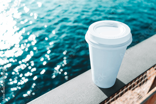 Absolutely white paper cup of coffee, located on the railing of the embankment parapet on a sunny day