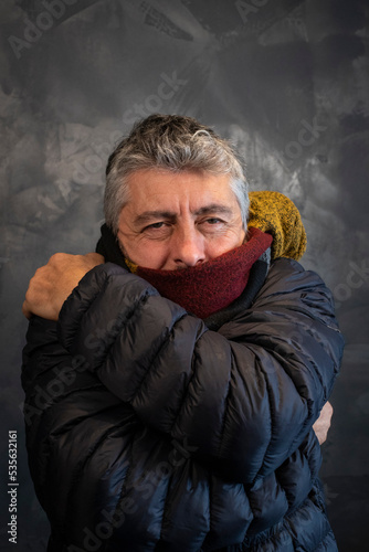 Homme malade qui a froid. il porte une écharpe, un gros manteau d'hiver dans sa maison et il grelotte photo