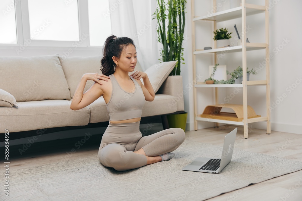 Young Asian woman in front of her laptop sports and yoga repeating exercises on the video at home in lotus position stretching the muscles of the neck, a set of home workouts for the body lifestyle Young Asian woman in front of her laptop sports and yoga repeating exercises on the video at home in lotus position stretching the muscles of the neck, a set of home workouts for the body lifestyle