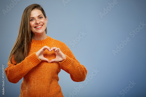 Smiling woman in warm orange sweater making heart with finger.