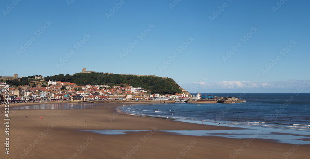 wide panoramic view of the town of Scarborough from south bay beach showing the Grand Hotel, castle and lighthouse and a sunlit blue sea wide panoramic view of the town of Scarborough from south bay beach showing the Grand Hotel, castle and lighthouse and a sunlit blue sea