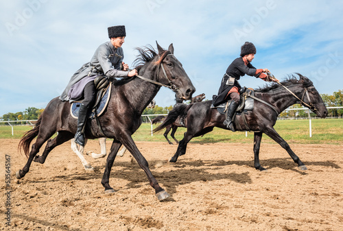 Two horsemen in national Caucasian costumes are rapidly galloping to the racetrack