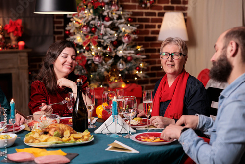 Woman and man celebrating christmas with parents, family sitting at festive dinner table at home party. People eating traditional xmas food, drinking sparkling wine, laughing