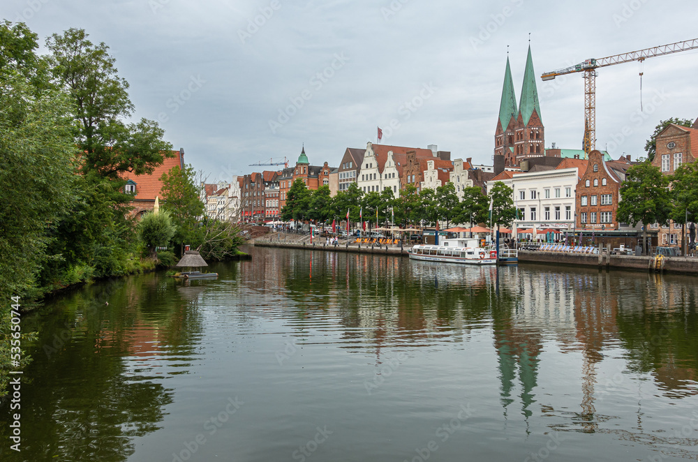 Germany, Lubeck - July 13, 2022: Marienkirche, mary churchesseen from over Trave river under gray cloudscape. historic architecture on quay. Crane disturbes scenery