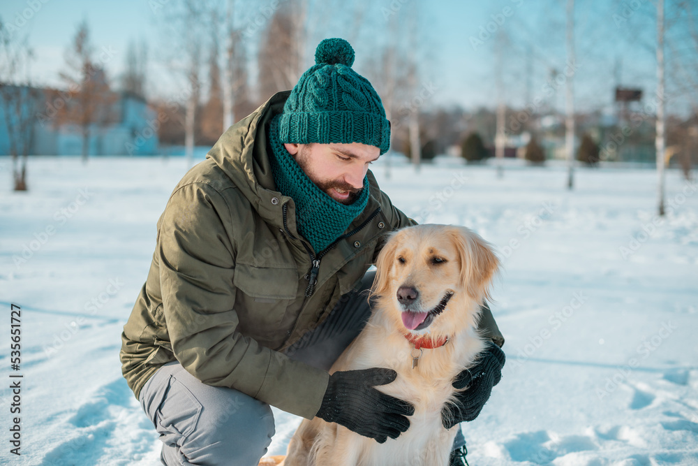 Golden retriever playing with his owner walking outdoors winter day, warm clothing. love and care for the pet.