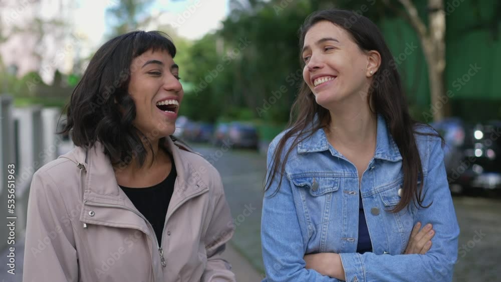Two happy female friends laughing and smiling while walking outside in street sidewalk Two happy female friends laughing and smiling while walking outside in street sidewalk