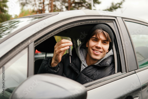 Young smiling man student holding key of new car. Rent car or buying first car concept. © glebcallfives