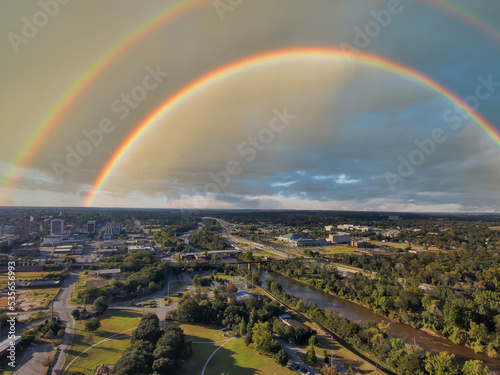 an aerial shot of a gorgeous autumn landscape at Carolyn Crayton Park at sunset with a river, lush green trees and buildings with blue sky, clouds and a rainbow in Macon Georgia USA photo