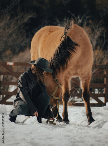 cowgirl petting her horse in the snow with hat and leather jacket on a cloudy day photo