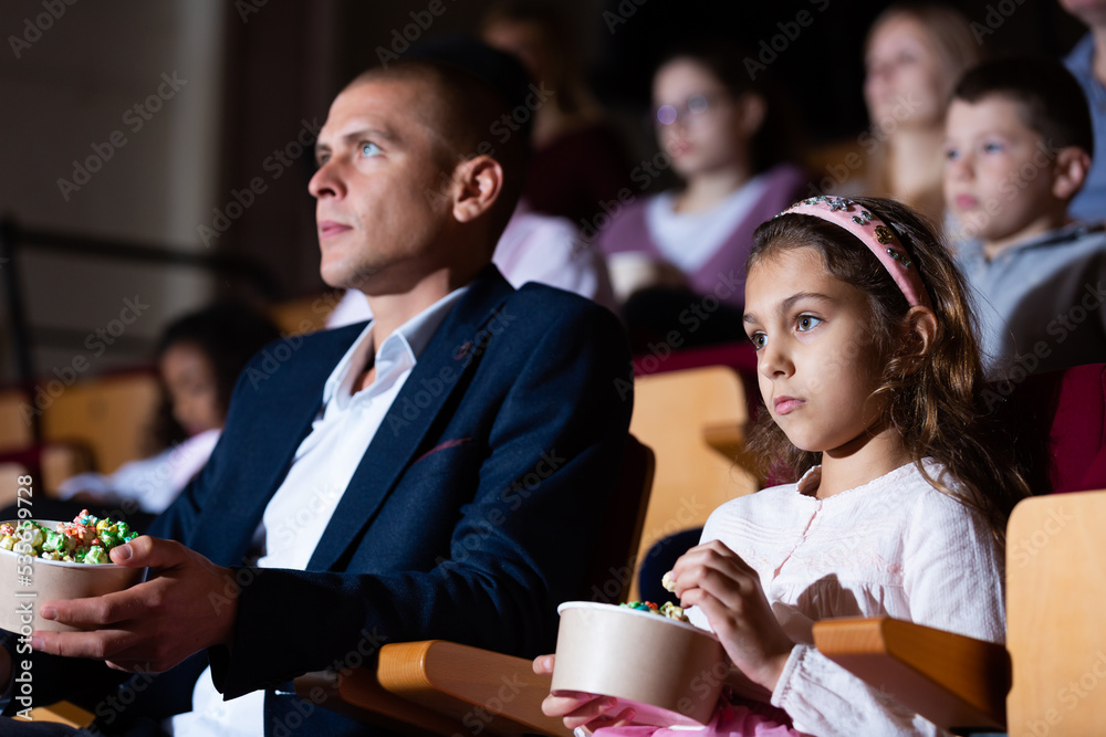 Portrait of tween girl visiting cinema with her father, enjoying watching interesting movie and eating popcorn