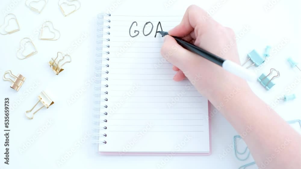Female hand writes goals in a notebook on white background close-up. Female hand writes goals in a notebook on white background close-up.