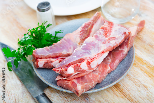 Fresh uncooked pork ribs on ceramic plate with parsley and kitchen knife. Ingredient for cook