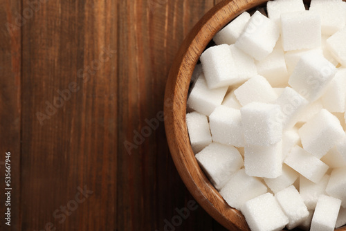Bowl with sugar cubes on wooden table, top view. Space for text