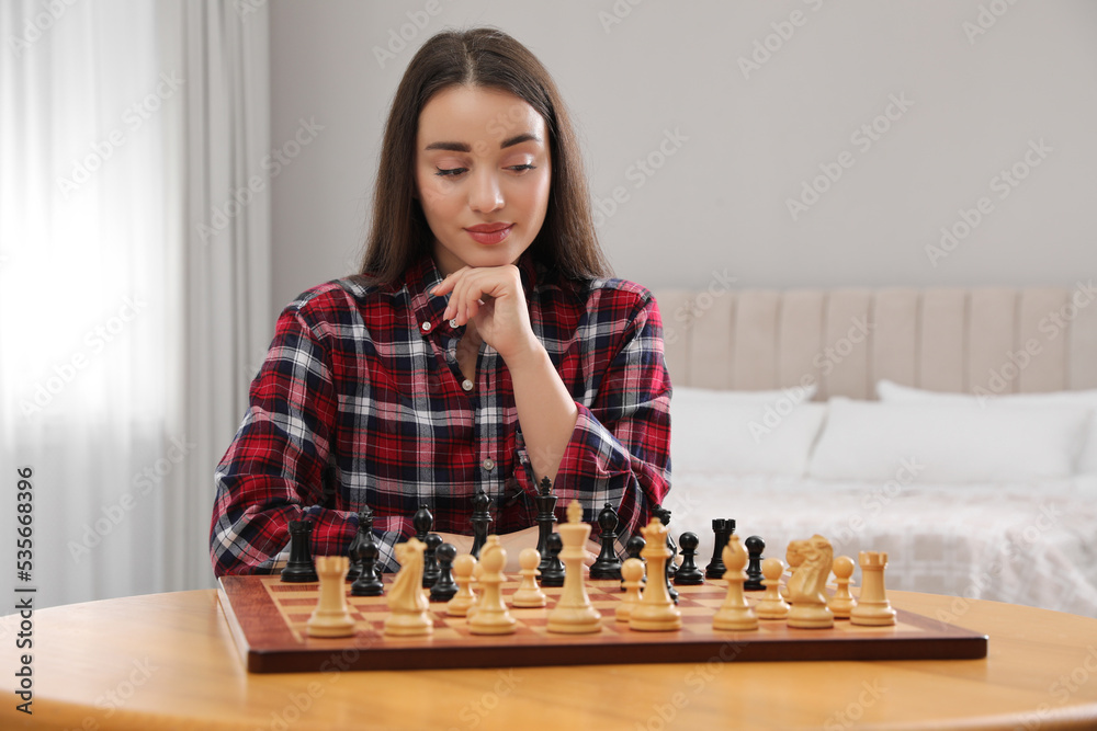 Young woman playing chess at table in bedroom Young woman playing chess at table in bedroom