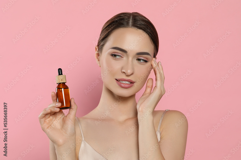 Fototapeta premium Young woman with bottle of essential oil on pink background