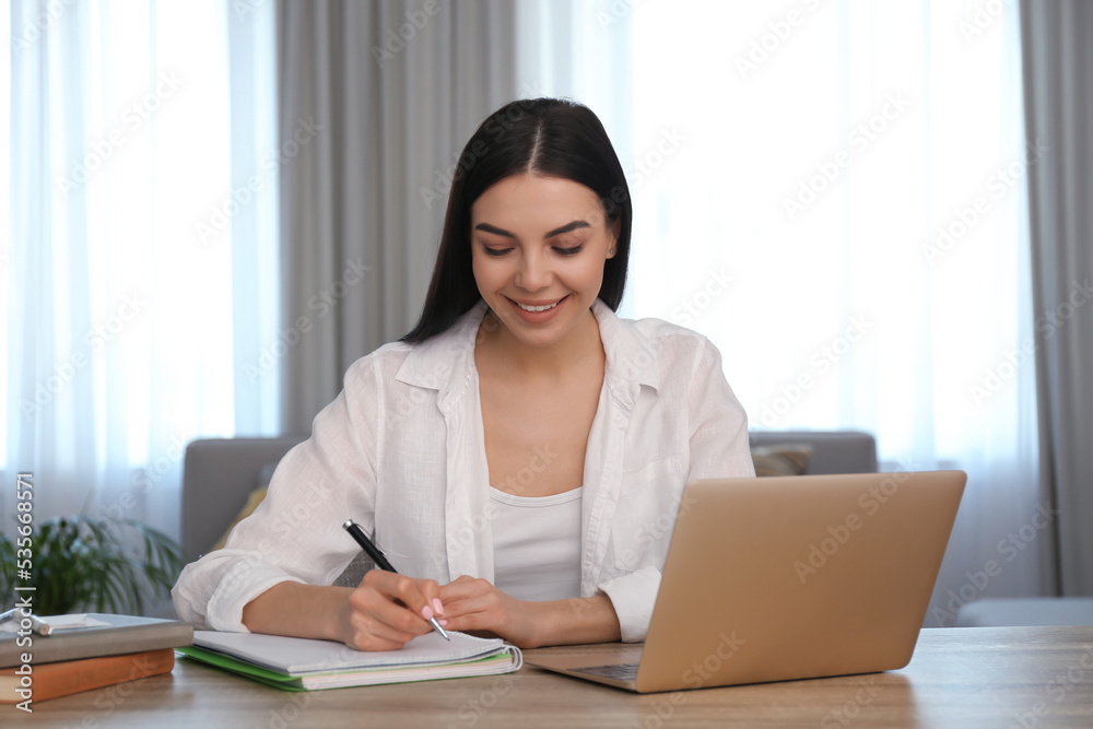 Young woman taking notes during online webinar at table indoors Young woman taking notes during online webinar at table indoors