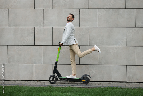 Businessman riding modern kick scooter near grey stone wall outdoors photo