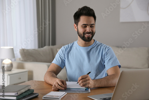 Young man watching webinar at table in room
