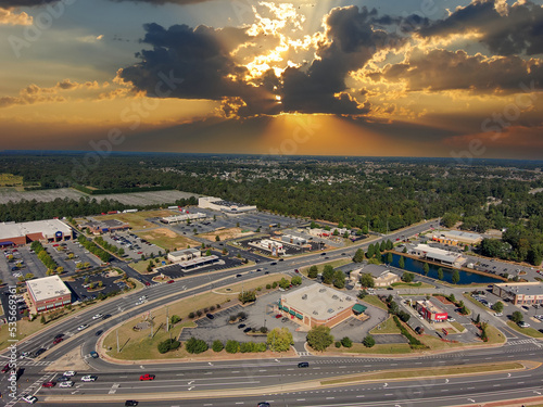 an aerial shot of the city of Warner Robins Georgia with vast miles of lush green trees, grass and plants with buildings and highways with cars driving and powerful clouds at sunset photo