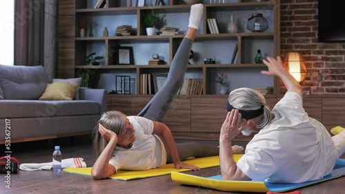 Gray-haired happy mature elderly couple doing gymnastics together at home. Active and healthy lifestyle for pensioners. Fitness, recreation, well-being of the elderly.