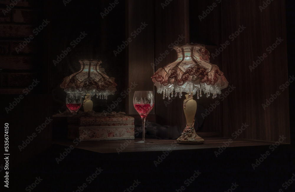 A glass of red wine in the dim light of Vintage lamp with reflection from mirror. Light and Shadow, Dark tone, Copy space, Selective focus.
