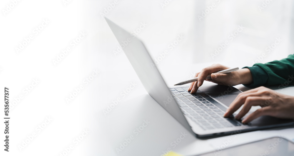 Close-up Businesswoman working online on the white table at office, hands holding pen and typing on laptop keyboard, online job concept. Close-up Businesswoman working online on the white table at office, hands holding pen and typing on laptop keyboard, online job concept.