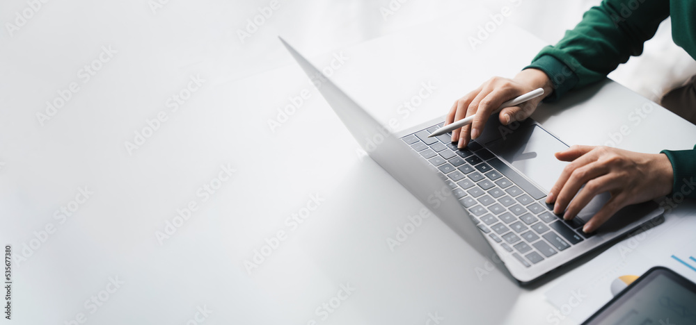 Close-up Businesswoman working online on the white table at office, hands holding pen and typing on laptop keyboard, online job concept. - obrazy, fototapety, plakaty 