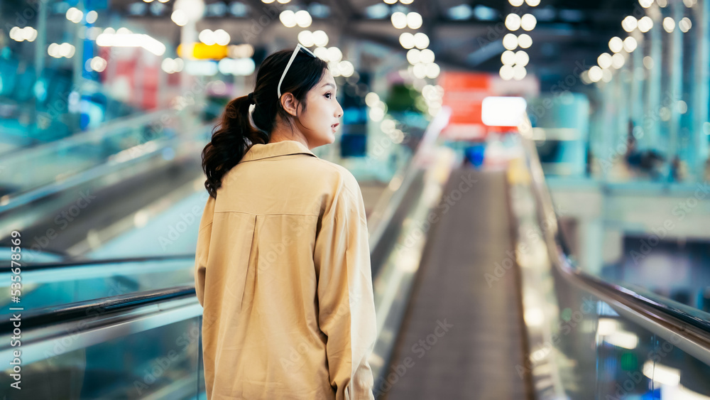 Young asian woman passenger in airport terminal or modern train station. Asia woman commuter travels with luggage on escalator