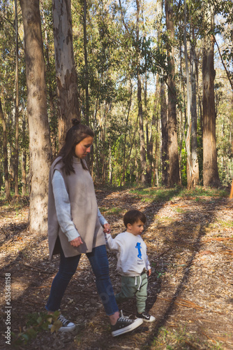 a young mother walks with her little son through a park and forest enjoying the sun and nature as a family with a maternity full of love