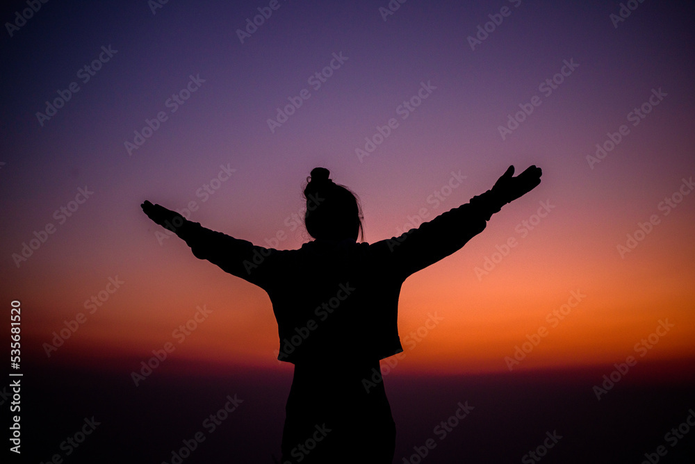 Silhouette of cheering hiking woman open arms to the sunrise stand on mountain