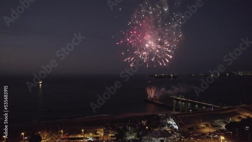 imagen aérea desde un dron de show pirotécnico. fuegos artificiales en el mar con explosiones y colores. Show lanzado desde muelle de pescadores. Se ve la ciudad iluminada de fondo photo