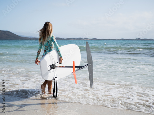 Young woman from behind walking to the water on the beach shore to practice hydrofoil surfing water sport photo