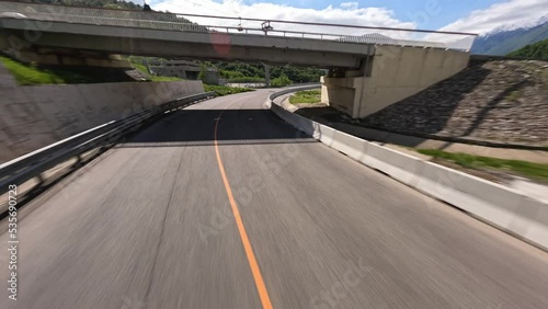 FPV sports drone top shot diving over empty serpentine asphalt road mountain alpine resort sunny landscape aerial view. Speed flight in bridge tunnel picturesque suburb city landmark infrastructure 4k photo