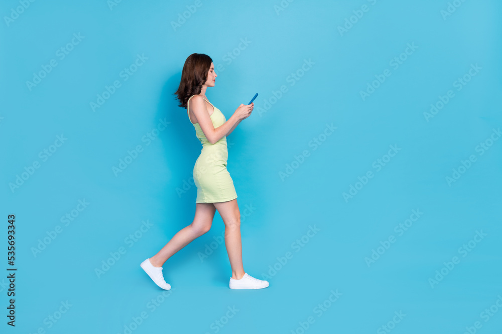 Obraz premium Full length photo of pretty cute girl dressed green clothes walking typing modern device empty space isolated blue color background